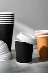 Stack of coffee cups in various colors with lids on a gray surface