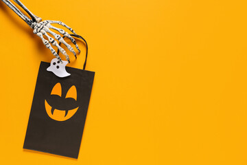 Skeleton hand with Halloween shopping bag on orange background