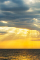 Fototapeta premium Orange sunrise sunrise over sea horizon. Sun rays light drop on colorful clouds on sky. vertical