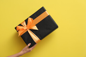 Female hand with Halloween gift box on yellow background