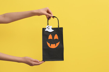 Female hands with Halloween shopping bag on yellow background
