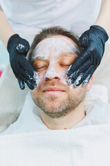 Naklejka premium A beautician applies a medical mask to a man's face. Facial skin care for men. Male cosmetology.