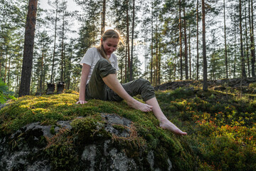 woman sitting on a stone with moss without shoes in the forest