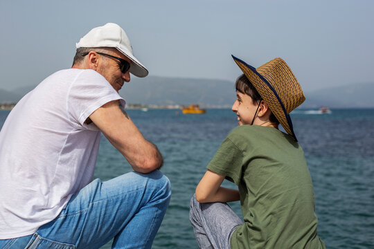 Father and son in a hats by the sea talking and smiling