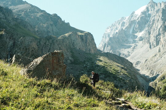 Adult man with a hiking backpack traverses mountainous landscape