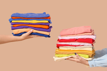 Young women with stacks of colorful clothes on beige background