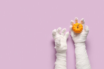 Mummy hands with pumpkin on purple background. Halloween celebration