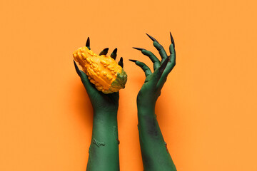 Green hands of witch with pumpkin on orange background. Halloween celebration
