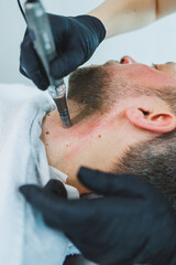 Fototapeta premium A cosmetologist cleans the skin of a man's face. A man does facial procedures in a cosmetic clinic. Male cosmetology.