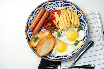 Breakfast plate with fried eggs, sausage, tomatoes, and fries served on a decorative blue plate