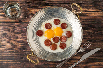 Eggs with Turkish sausage in a copper pan on a wooden table. Turkish name sucuklu yumurta