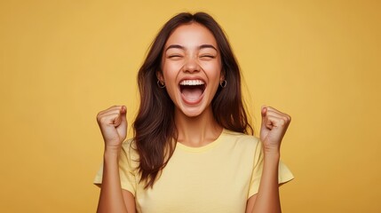 Excited woman in yellow t-shirt celebrating and cheering against a yellow background, expressing joy and happiness.