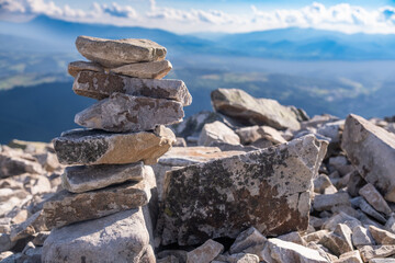 Stacked stones forming a cairn on a mountain summit with expansive views of distant valleys and peaks during daylight