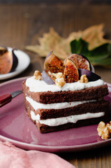 Piece of chocolate cake with nuts, violet figs and whipped cream on violet-pink plate. On vintage background for autumn concept. 