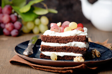 Close up of chocolate cake with fresh grapes and whipped cream on blue plate. On background with Grapes.