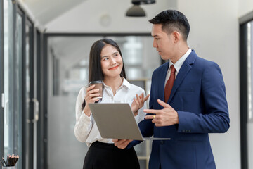 A professional setting where a man and woman engage in conversation while holding a laptop and a coffee cup.