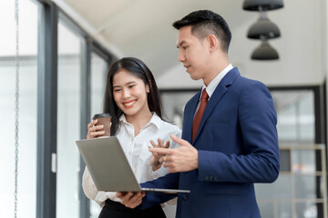A woman and a man discuss work matters with a laptop in a modern office setting, both engaged and smiling.