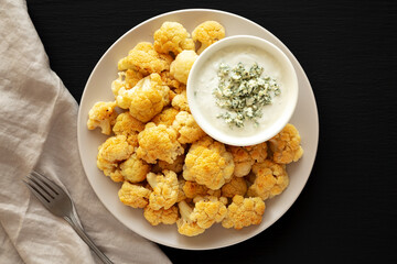 Homemade Buffalo Cauliflower with Blue Cheese Sauce on a Plate on a Black Background, top view.