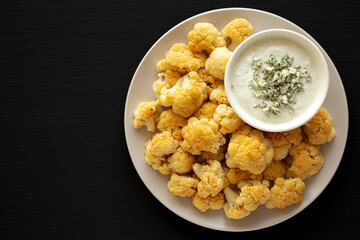 Homemade Buffalo Cauliflower with Blue Cheese Sauce on a Plate on a Black Background, top view. Copy space.