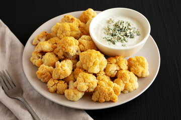 Homemade Buffalo Cauliflower with Blue Cheese Sauce on a Plate on a Black Background, side view.