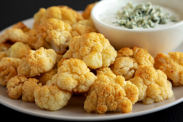 Homemade Buffalo Cauliflower with Blue Cheese Sauce on a Plate on a Black Background, side view. Close-up.