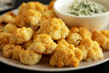 Homemade Buffalo Cauliflower with Blue Cheese Sauce on a Plate on a Black Background, side view. Close-up.