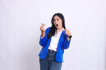 beautiful adult office girl wearing blue formal suit standing surprised to camera holding bitcoin while pointing at it isolated white background. for transaction, investment, business content