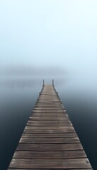 Fototapeta premium A weathered wooden pier extends out into a still, foggy lake, with trees displaying brilliant autumn colors lining the far shore.