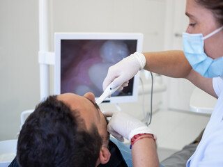 A dental professional is using an intraoral camera to examine a patient's teeth. The setting is a...