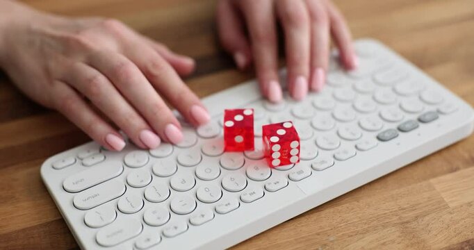 Female hand with nude manicure puts red dices on white keyboard lying on wooden table. Red transparent ivories with equal dots on portable keypad. Fortune concept
