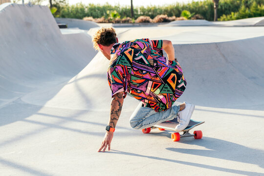 back view of anonymous funky young male skateboarder in trendy colorful shirt and jeans performing trick on concrete ramp while practicing skills in skatepark