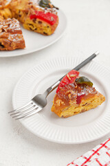 A slice of colorful cake with candied fruit and a fork on a white plate, paired with a checkered napkin