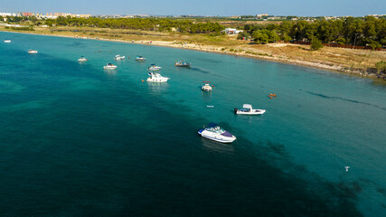 Aerial view of a group of boats anchored near a beach in Puglia, Italy. The sea is crystal blue.
