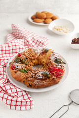 A wreath shaped cake with candied fruit and nuts on a white plate, surrounded by bowls and napkins