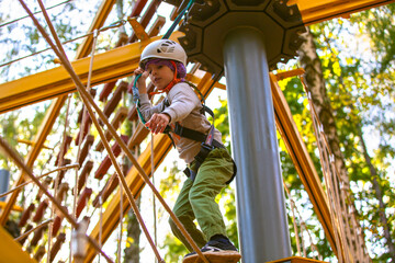 brave little boy in helmet climbing at adventure park in autumn season. Work out concept