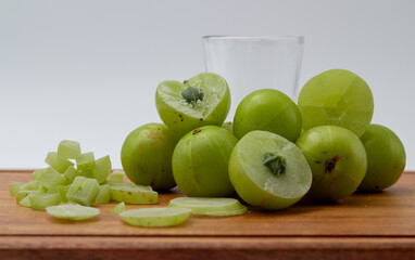 A glass of Amla juice ,chopped amla and whole amla also known as Indian gooseberry placed on a wooden chopping board.