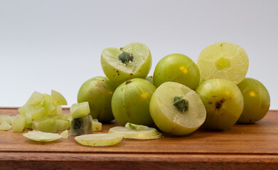 Chopped amla and whole amla also known as Indian gooseberry placed on a wooden chopping board.