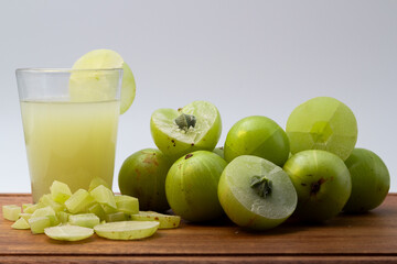 A glass of Amla juice ,chopped amla and whole amla also known as Indian gooseberry placed on a wooden chopping board.