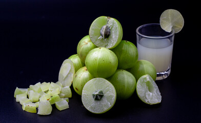 A glass of Amla juice ,chopped amla and whole amla also known as Indian gooseberry placed on a wooden chopping board.