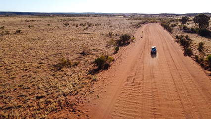Aerial picture of a car driving in the middle of the outback. Long sandy road with bushes on the side. 4x4 adventure in the red centre of Australia. © Elsa