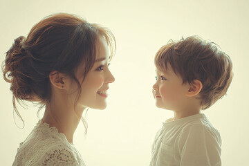 Young Chinese mother and cute son interacting and smiling in front of a plain background, dressed in simple clothes, during a family photo portrait shoot.