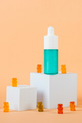 Blue glass cosmetic bottle, Skin care or sunscreen cosmetic with stylish props and fruit gummi on cream background.