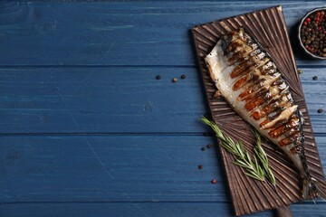 Board with delicious grilled mackerel, peppercorns and rosemary on blue wooden table, flat lay. Space for text