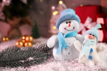 Funny snowmen figures and fir branch on artificial snow, closeup