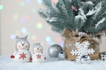 Cute snowmen, Christmas balls and fir branches against beige background with blurred lights, bokeh effect