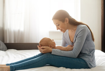 In a cozy bedroom filled with natural light, a mother sits on the bed, gently cradling her newborn...