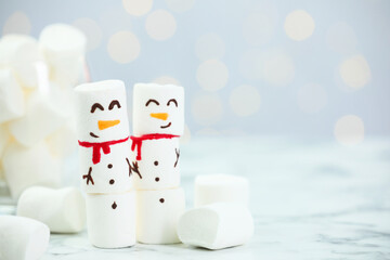 Funny snowmen made with marshmallows on white table against blurred lights. Space for text