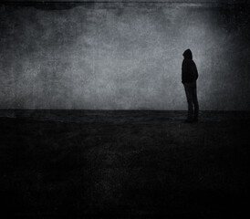 Dark grungy  textured image of person in silhouette looking out over the sea.