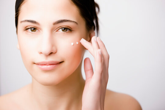 Close up of a young woman applying moisturizer on her cheek
