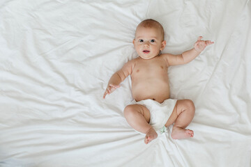 A cute baby appears content and playful while lying on a clean, soft white blanket. The bright atmosphere emphasizes the baby's cheerful expression.